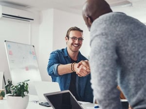 A photo of two men smiling and shaking hands